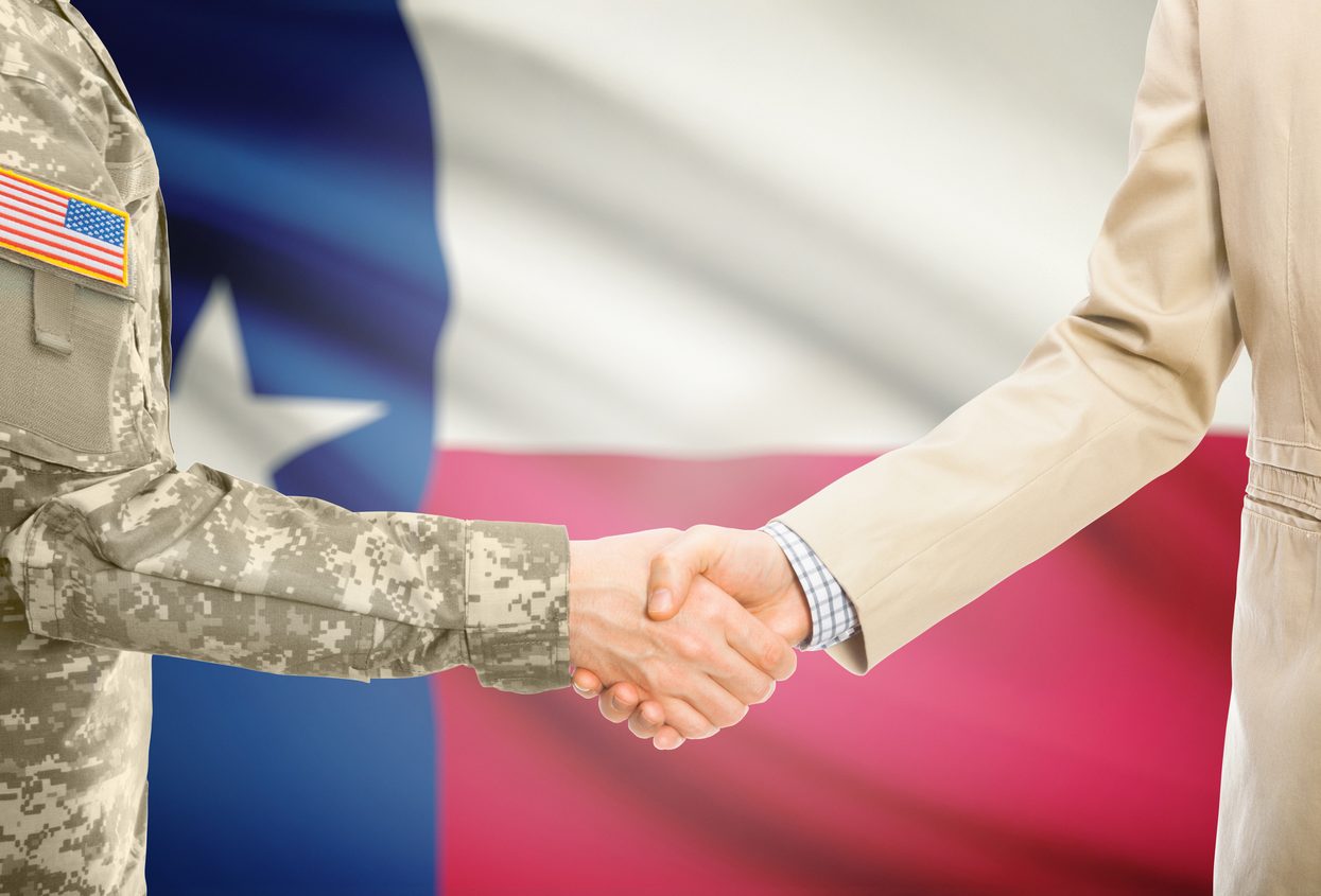 Soldier in uniform and businessman in suit shaking hands in front of the Texas flag